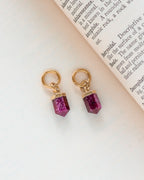 Interchangeable hoop earring charms with ruby pendants attached to gold hoops, on a paper with text.