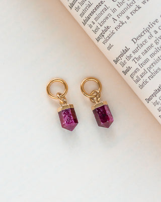 Interchangeable hoop earring charms with ruby pendants attached to gold-colored hoops, displayed on a paper with text.