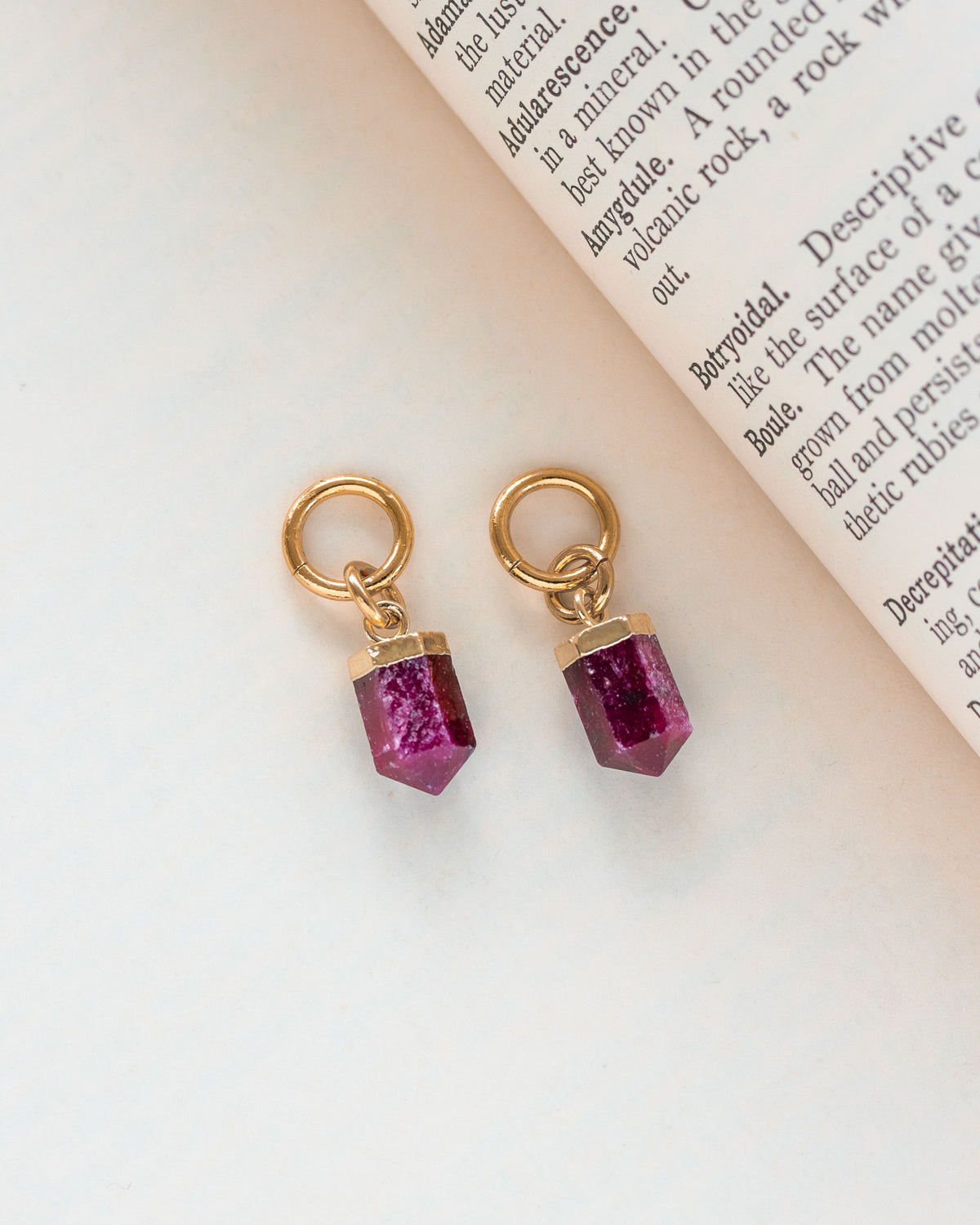 Interchangeable hoop earring charms with ruby pendants attached to gold hoops, on a paper with text.
