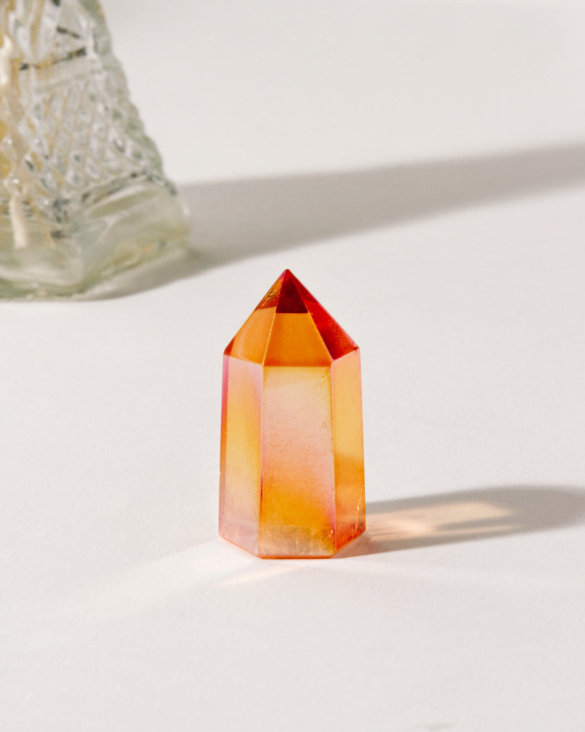 Tangerine quartz mini tower crystal with a faceted point sits on a white surface with long shadows.