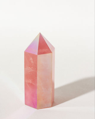 A pink iridescent crystal point tower with a faceted pyramid top, standing on a white surface with a soft shadow to the right.