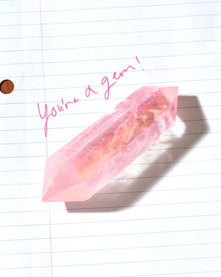 A pink pointed crystal point resting on lined notebook paper with pink handwritten text reading 'You're a gem!'.
