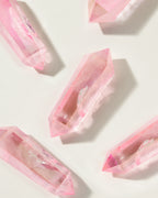 Overhead shot of several vibrant pink Pop Star Quartz double point crystals on a light background.