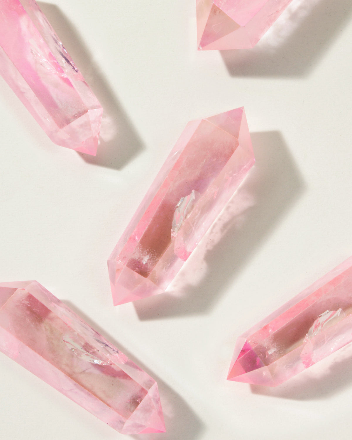 Overhead shot of several vibrant pink Pop Star Quartz double point crystals on a light background.