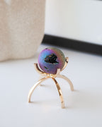 Rainbow druzy gemstone sphere on a gold tripod stand.