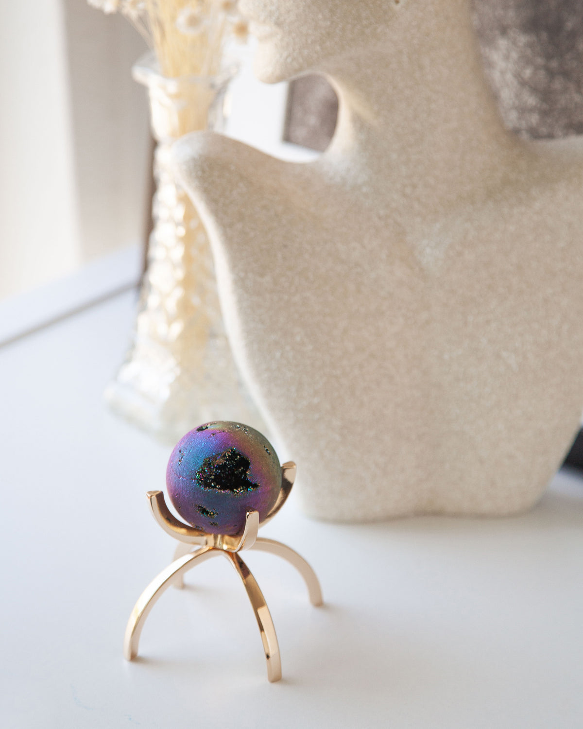 Rainbow druzy gemstone sphere on a gold stand.