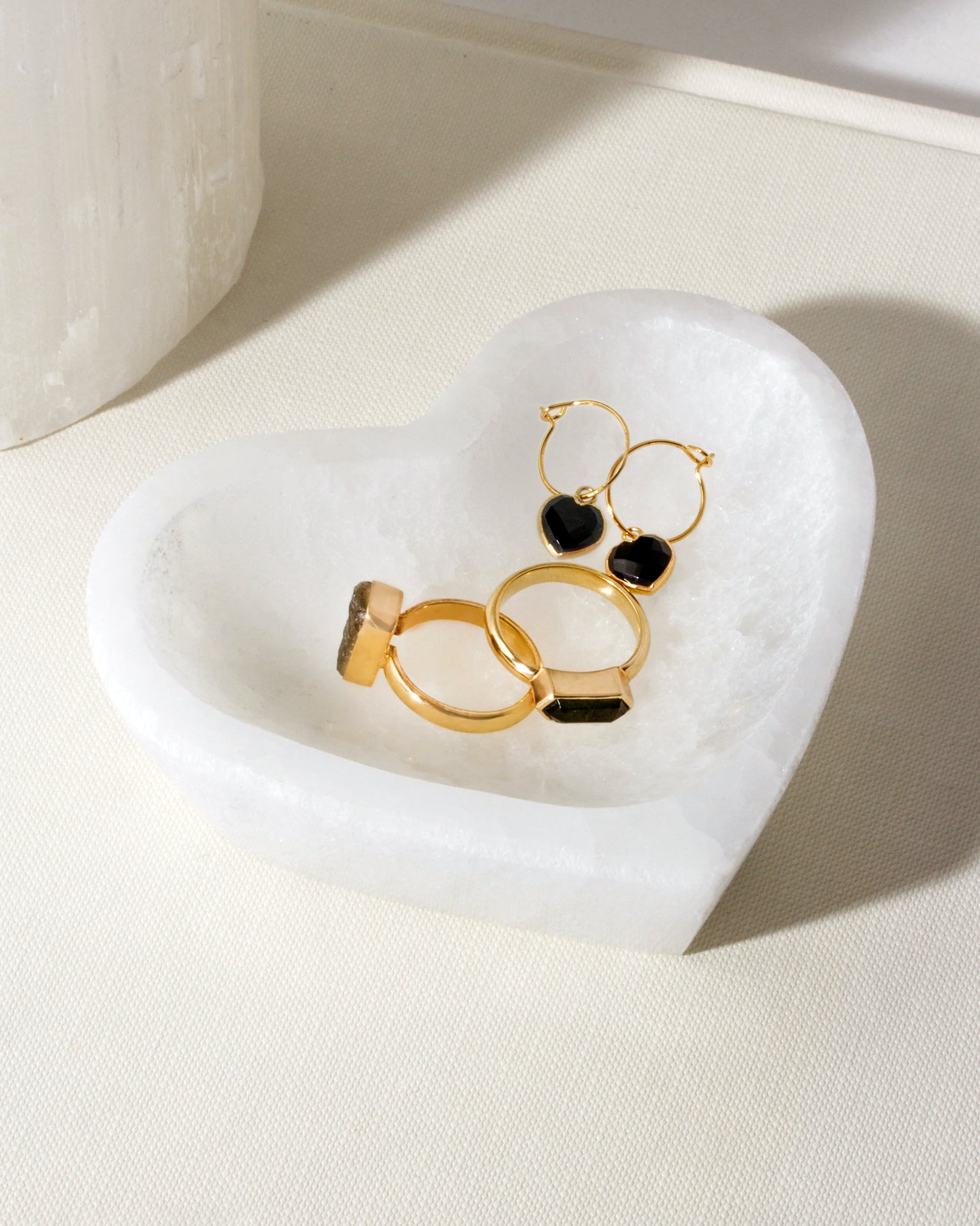 Heart-shaped white catchall holding two gold rings and black heart earrings.