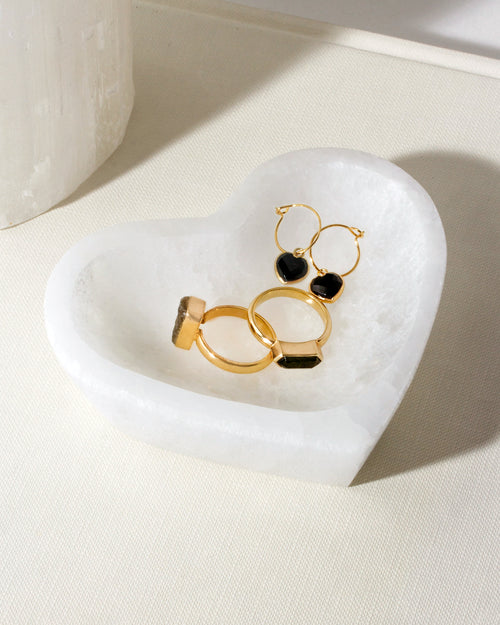 Heart-shaped white catchall holding two gold rings and black heart earrings.