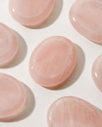 Many smooth rose quartz stone with a slight indent, placed on a white surface.