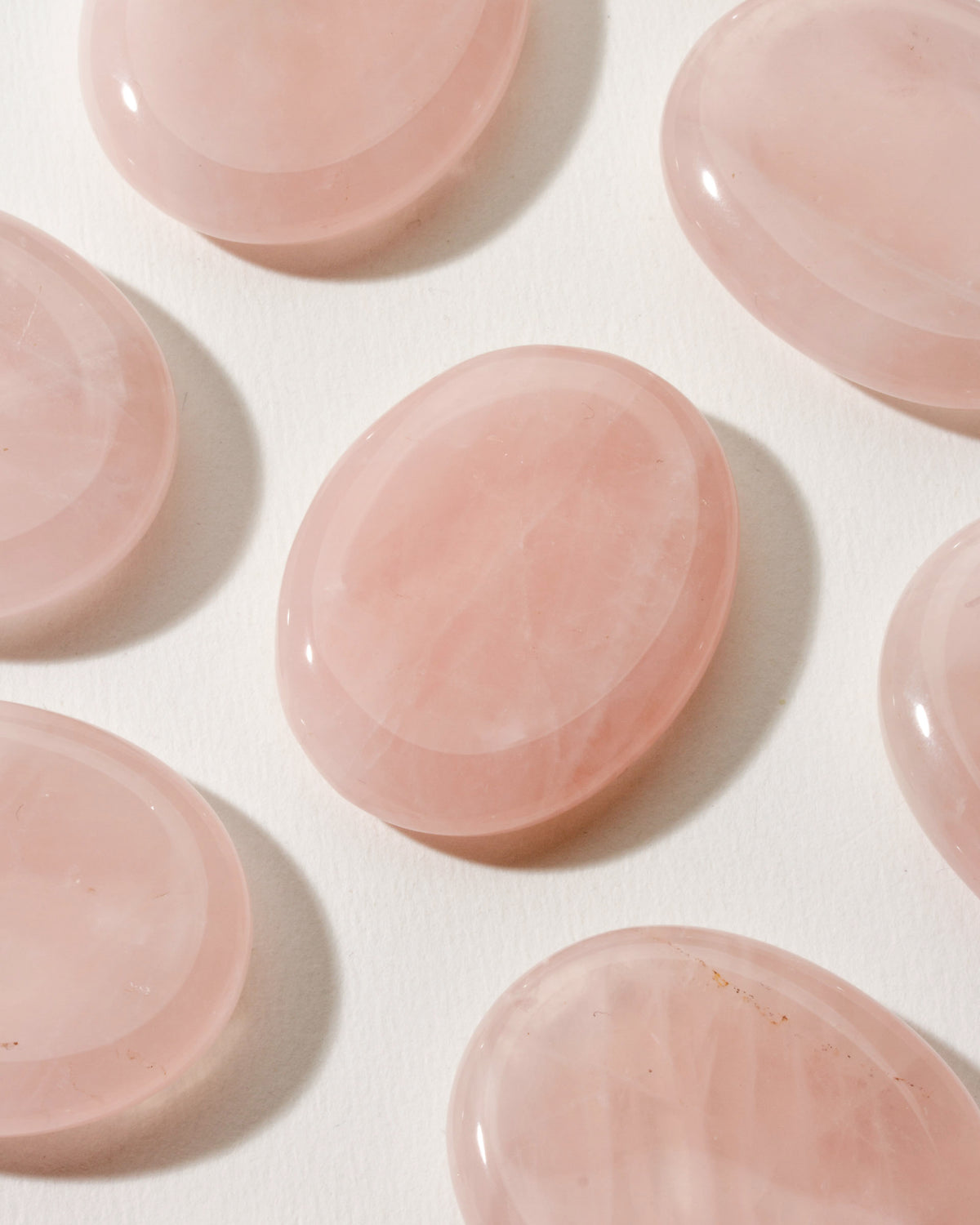 Many smooth rose quartz stone with a slight indent, placed on a white surface.
