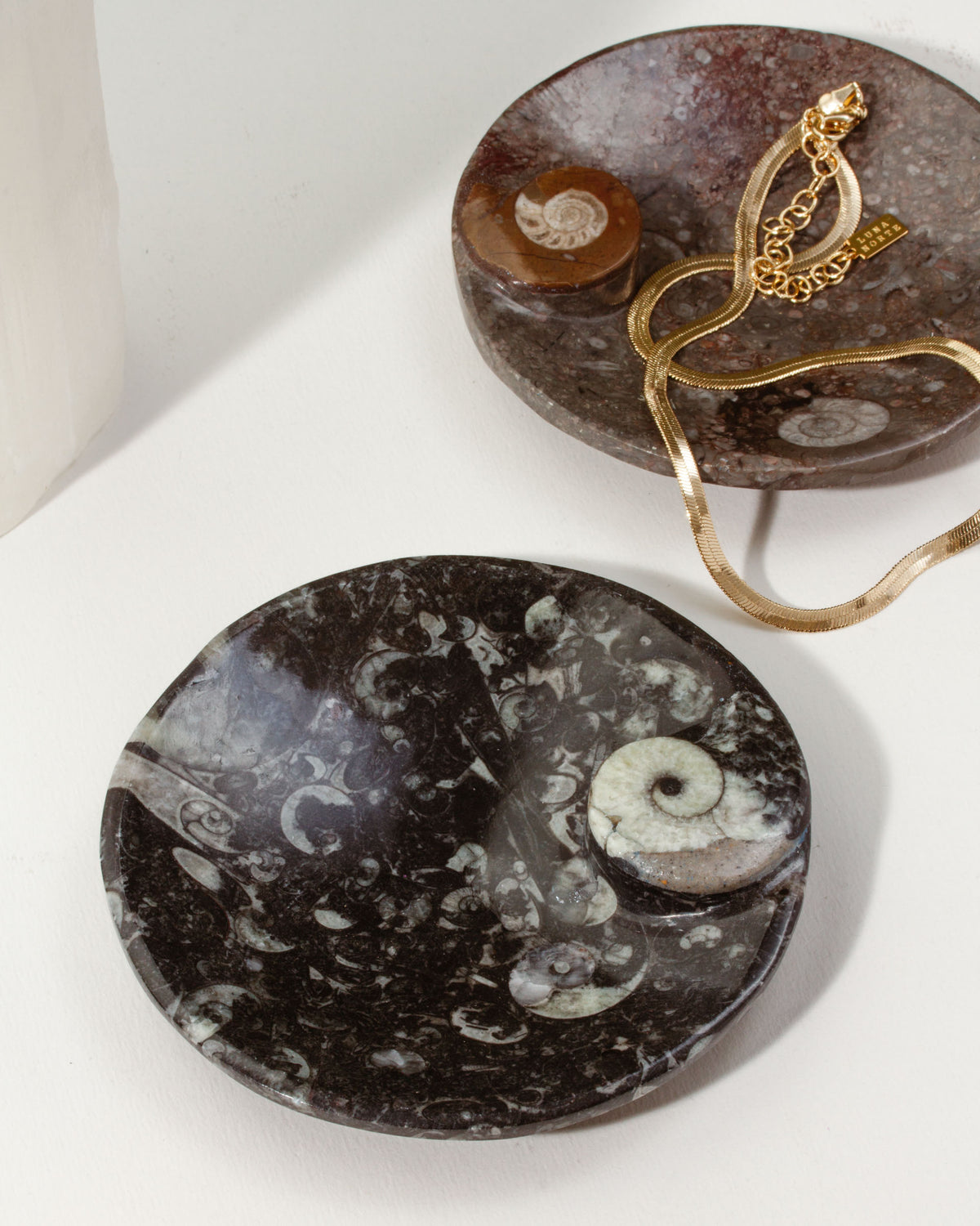 Black Journey of Life catchall, with a gold chain necklace draped on a brown catchall.