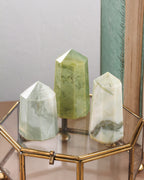 Three green crystal formations on a gold stand with a neutral background
