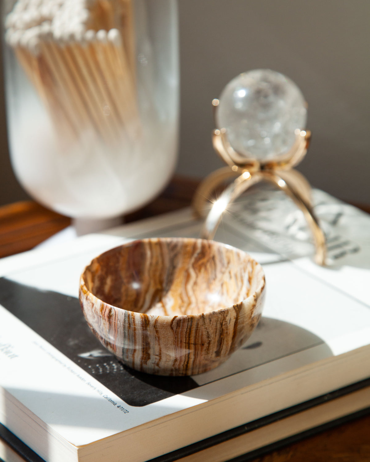 Carved Jumpstart Calcite Jewelry Bowl sits atop a book, with its brown-and-cream striped pattern.