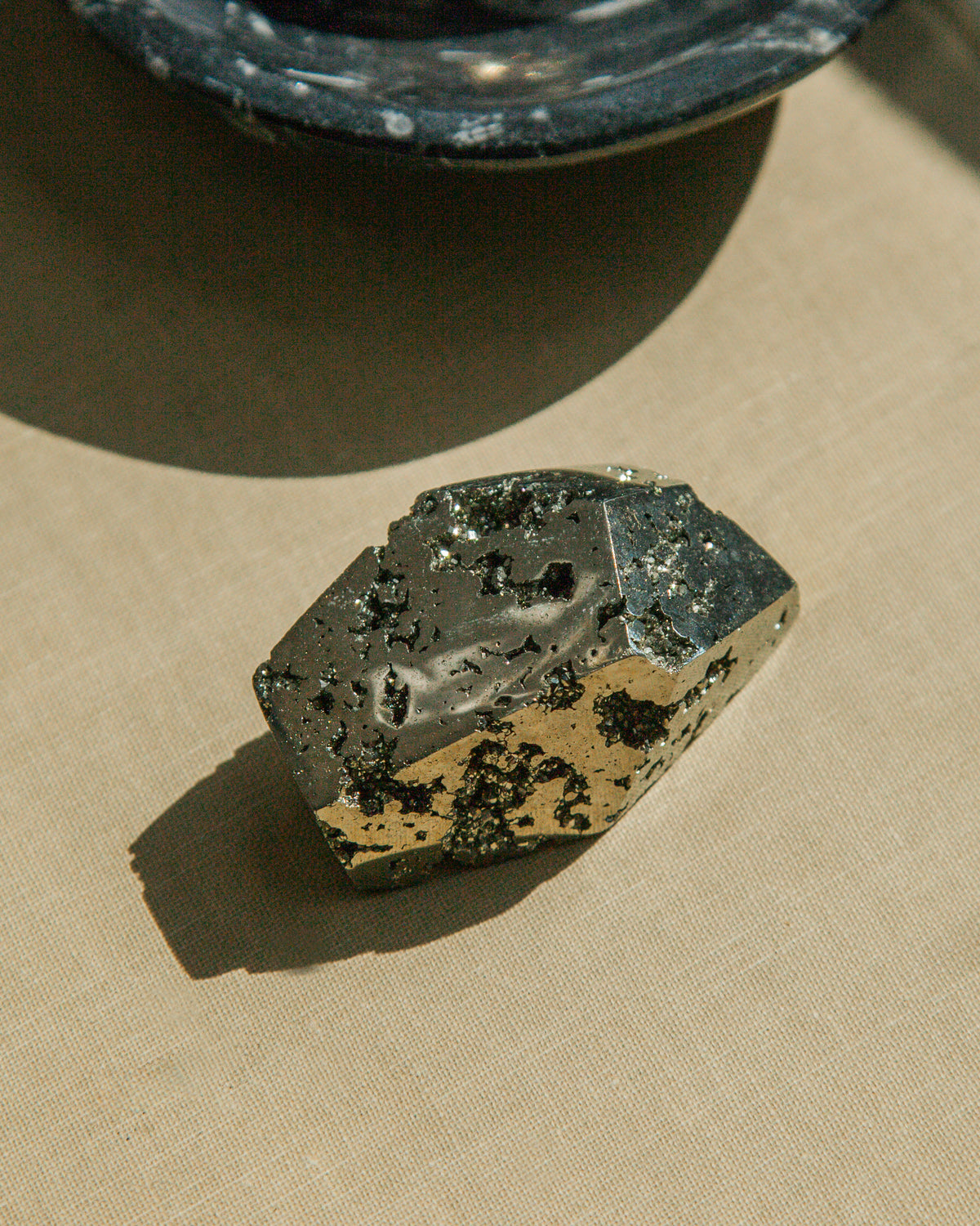 Faceted pyrite stone with metallic gold and dark gray hues on a textured surface.