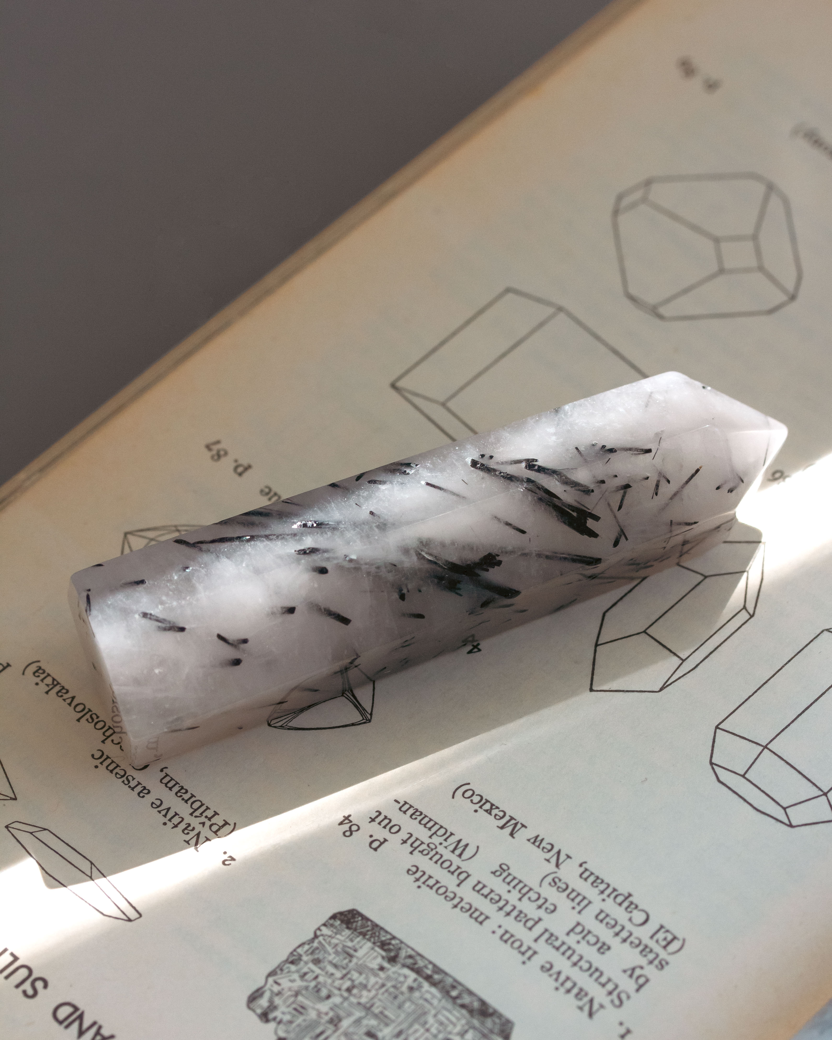 Tourmalinated quartz crystal tower on top of a book with crystal drawings.