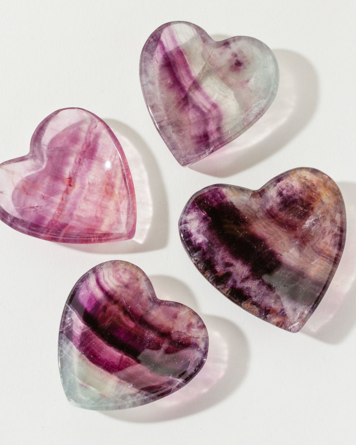 Four heart-shaped Rainbow Fluorite stones sit on a white surface.