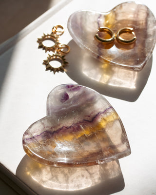 Two Heart-shaped Two heart-shaped Rainbow Fluorite bowls with gold jewelry on a white surface