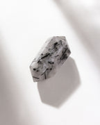 Tourmalinated quartz is clear with black tourmaline needles, casting a shadow on a white background.