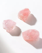 Three rose quartz stones are shown on a white surface.