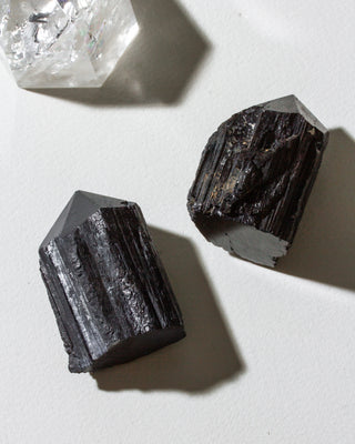 Two dark crystals on a light surface with a clear crystal in the background.