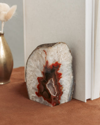 Geode bookend with red and brown interior on a surface next to a vase.