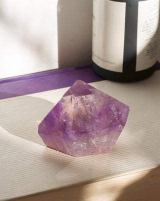 Amethyst crystal on a wooden surface with a bottle in the background
