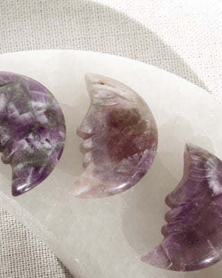 Three amethyst crystal face carvings on a white stone surface.
