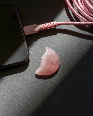Pink phone case and cable with rose quartz carved moon face gemstone on a dark surface