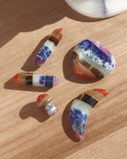 Five colorful multilayered gemstone crystal wands, mushroom, moon, and heart on a wooden table.