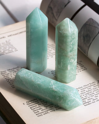 Three light mint crystal points arranged on an open book. The crystals have a soft minty blue-green hue with natural white veining.