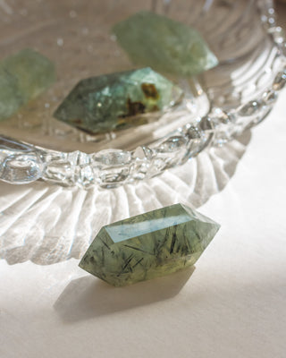 Green crystal on a white surface with a decorative glass dish in the background