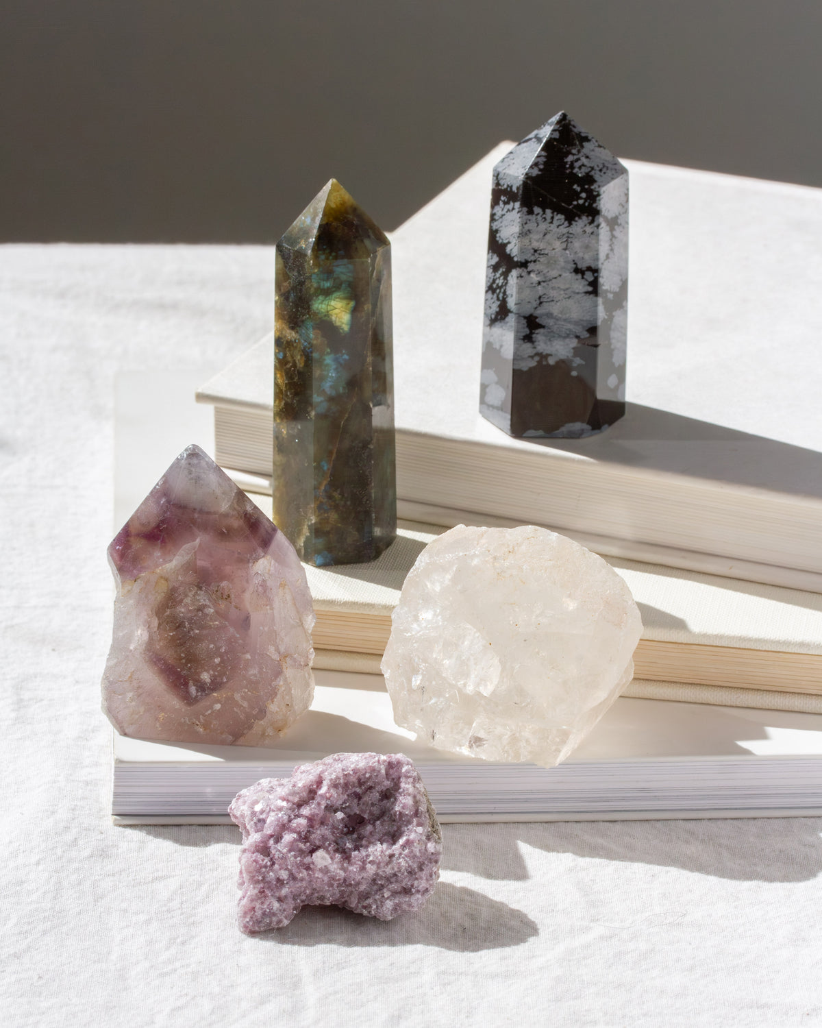 Various crystal towers and rough cut gemstones with a labradorite tower, stacked on top of books.