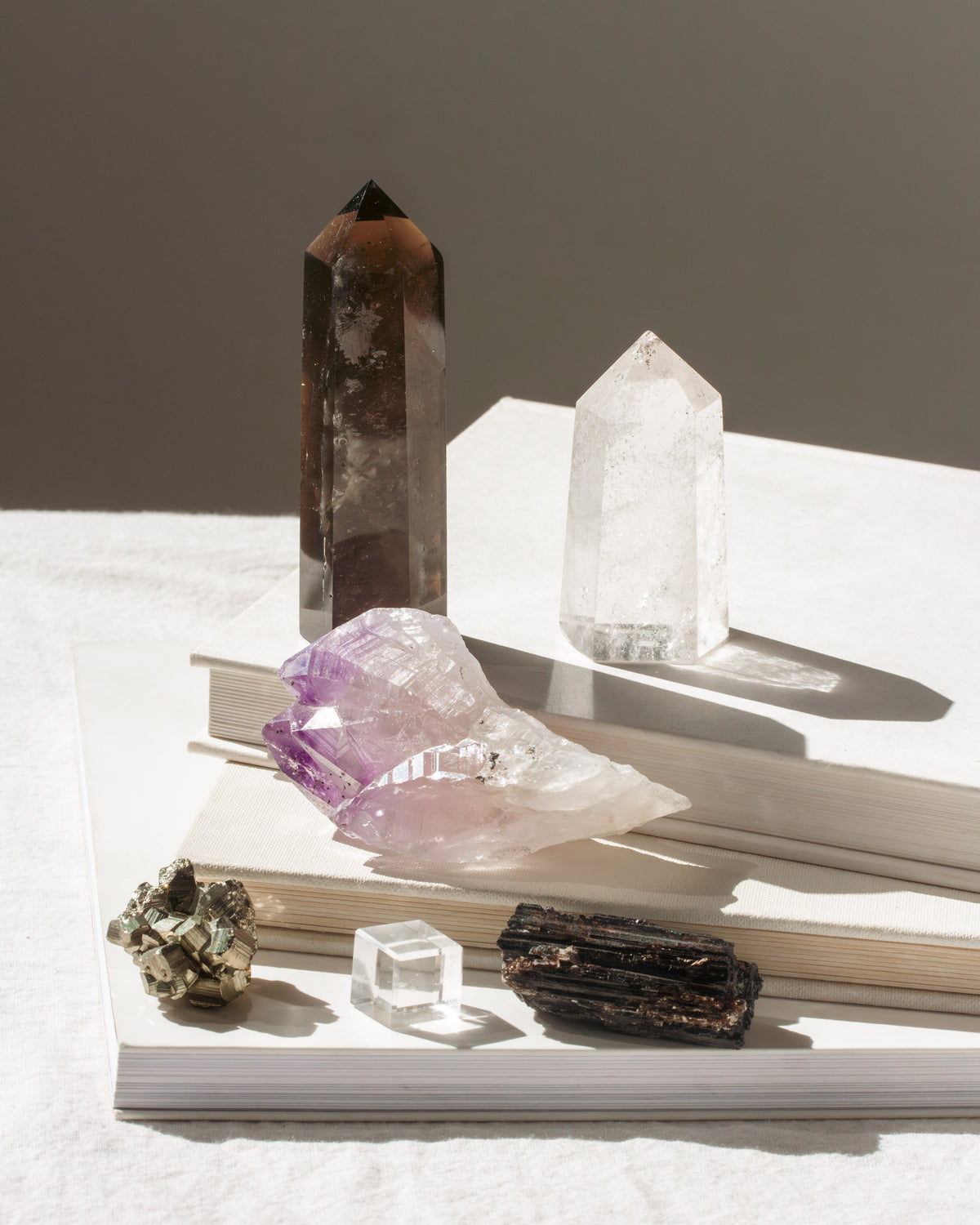 Variety of gemstone wands and rough gems on books, with smoky quartz and amethyst clusters