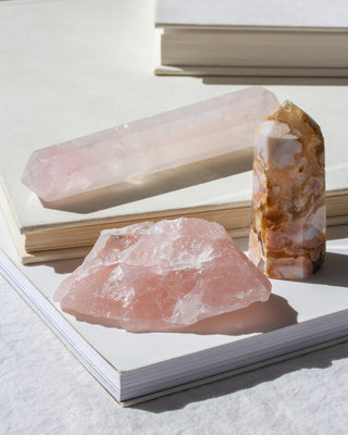 Three gemstones including rough Rose Quartz and two wands placed on top of books.
