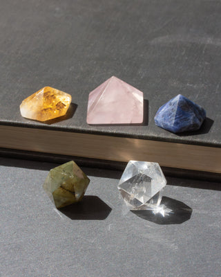 Variety of gemstone curios in many geometric shapes. This curated assortment includes faceted miniature gemstones of citrine, rose quartz, sodalite, alongside a clear quartz and labradorite & octahedron crystals. Though petite in size, each piece offers its own unique character, showcasing the remarkable colors, patterns, flashes, and formations found within genuine stone.