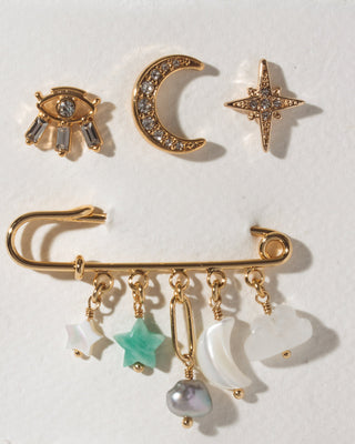 A set of celestial-themed gold-toned pins and a safety-pin style with dangling charms, including crescent moons, stars, and a pearl.
