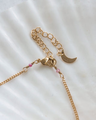 Gold necklace clasp detail with a moon charm on a white surface