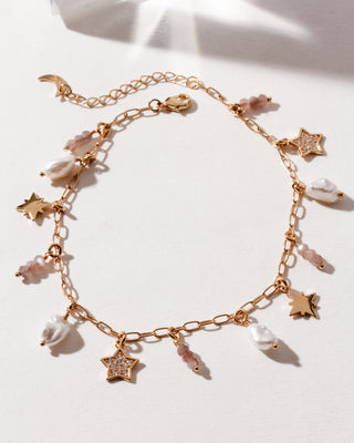 Gold plated anklet on a white surface with many gold, cz, pearl, and coffee moonstone beads and star charms; on a white surface.