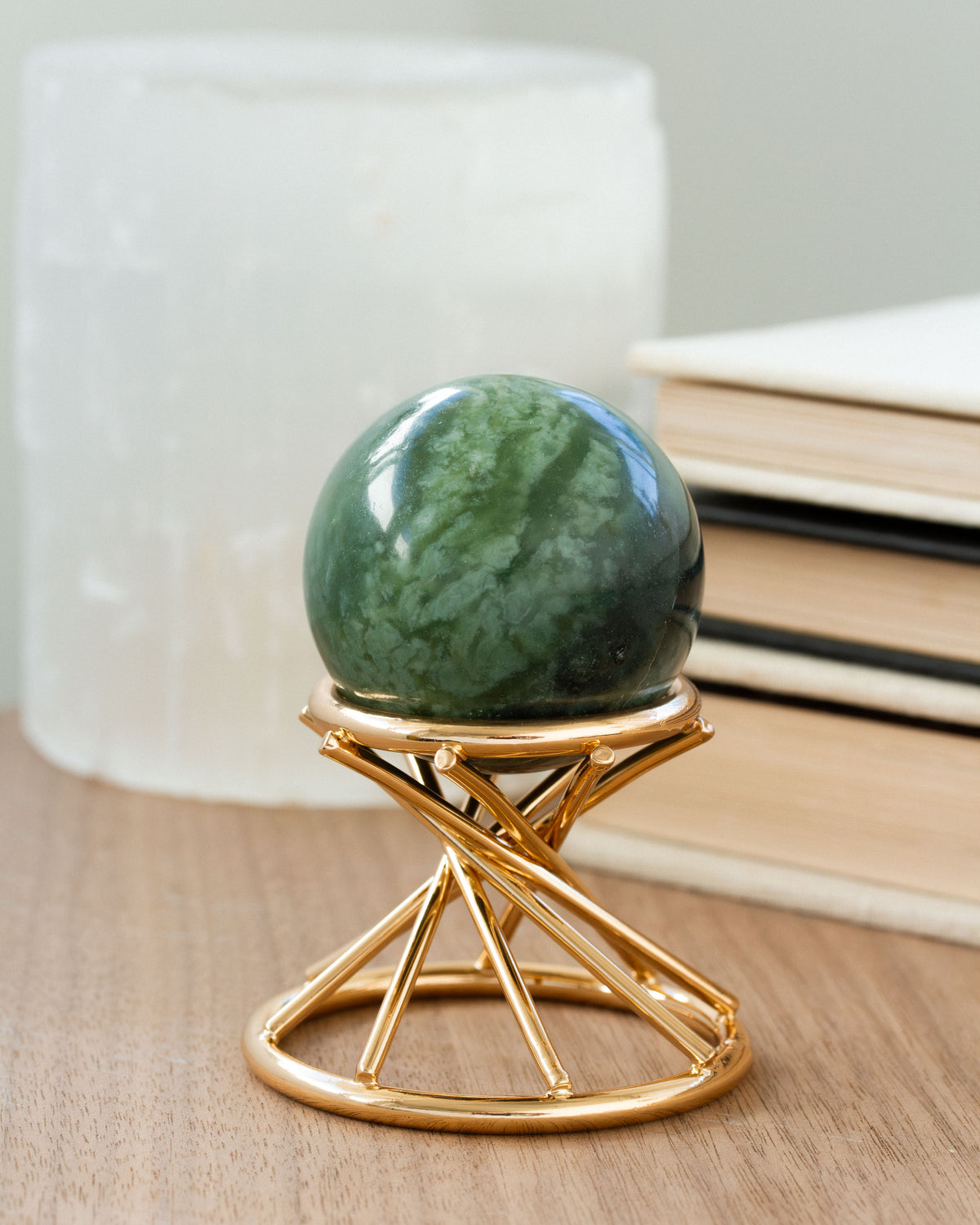 A green serpentine gemstone sphere on a gold geometric stand