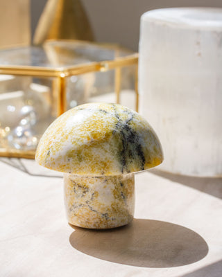 A mushroom or toadstool-shaped Serpentine gemstone with forest-like colors, placed on a flat surface with a shadow cast on the surface.