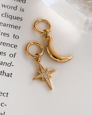 Two gold-colored interchangeable earring charms, one shaped like a crescent moon and the other like a star, placed against a backdrop of text.
