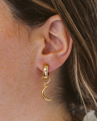 Person wearing a gold plated hoop earring in shape of a crescent moon.
