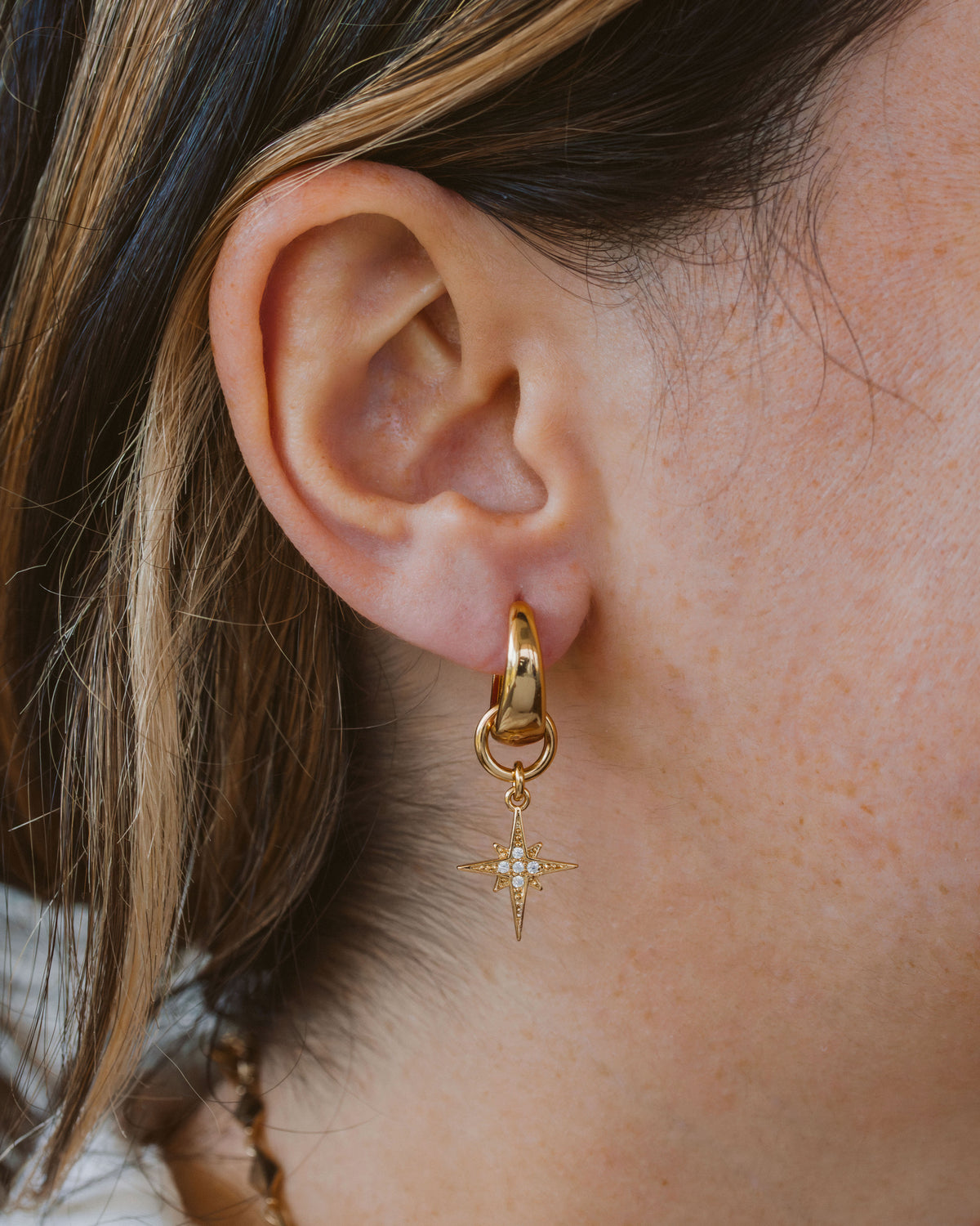 Close up of a person wearing a gold and cz star hoop earring.