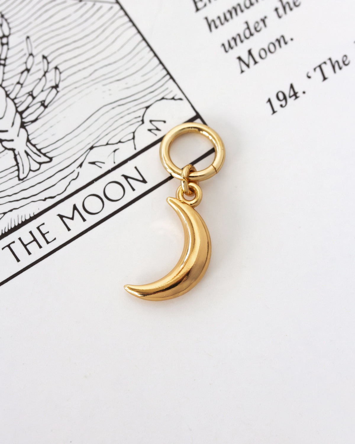 Gold-plated crescent moon hoop earring on a Moon tarot card page