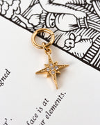 Gold star shaped interchangeable earring charm with cz elements laying on a book page.