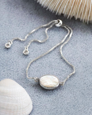 Silver bracelet with a central mother of pearl on a textured gray surface with shells.