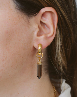 Model wearing a smoky quartz crystal charm with gold-colored caps and loops.
