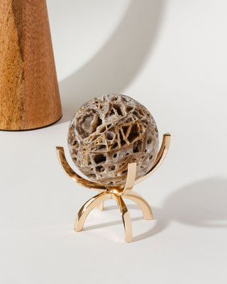 A sphalerite gemstone sphere with a veined texture and marbled earth tones, displayed on a gold-colored four-pegged stand.