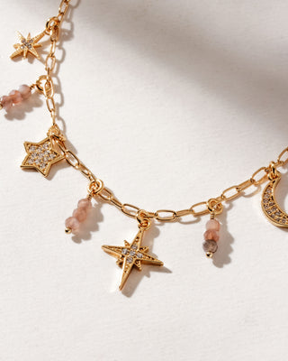 Detail of gold chain necklace with many star, and coffee moonstone beads on a white surface.