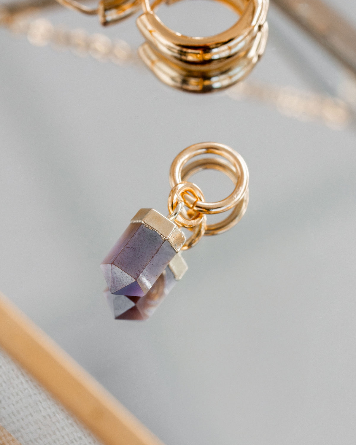 Coffee moonstone earring faceted pendant with gold hoop on a mirrored surface.